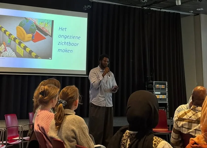 Foto van de middag in Wereldmuseum Leiden, met een spreker voor het scherm en publiek in de zaal.